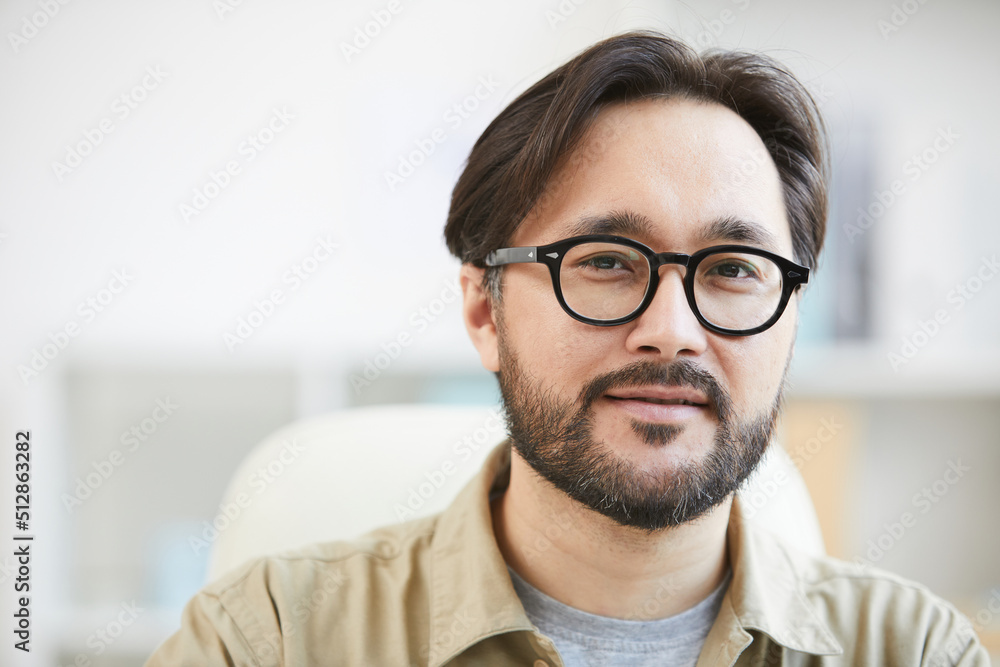 Close-up of content intelligent young Asian man with beard wearing eyeglasses working in office Close-up of content intelligent young Asian man with beard wearing eyeglasses working in office