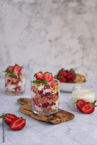 Tiramisu summer dessert with fresh strawberries and cream in a glass on a light gray marble background. Strawberry cream dessert in glasses, white background.