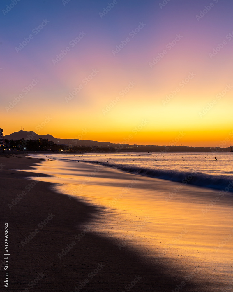 A vibrant sunrise with light reflecting in waves on the coastline of Médano beach in Cabo San Lucas 