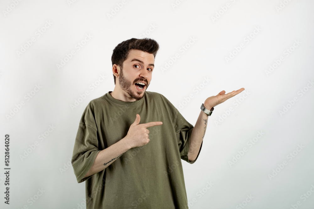 Cheerful caucasian man wearing casual clothes posing isolated over white background smiling while pointing with finger to his empty open hand palm. Cheerful caucasian man wearing casual clothes posing isolated over white background smiling while pointing with finger to his empty open hand palm.