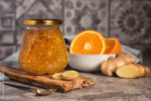 Homemade jam. A glass jar of orange-ginger jam on a gray background. Homemade orange and ginger marmalade and fresh oranges and ginger on the gray kitchen table. photo