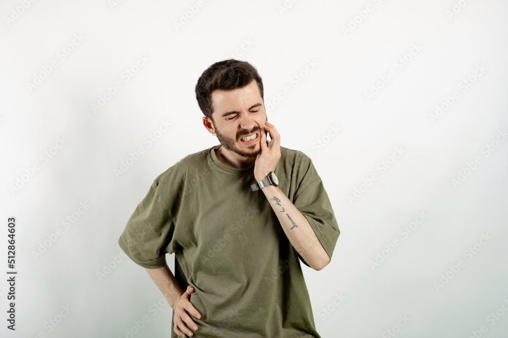 Portrait of young caucasian man wearing t-shirt posing isolated over white background feeling pain, holding his cheek with hand, suffering from bad toothache. Painful expression. Portrait of young caucasian man wearing t-shirt posing isolated over white background feeling pain, holding his cheek with hand, suffering from bad toothache. Painful expression.