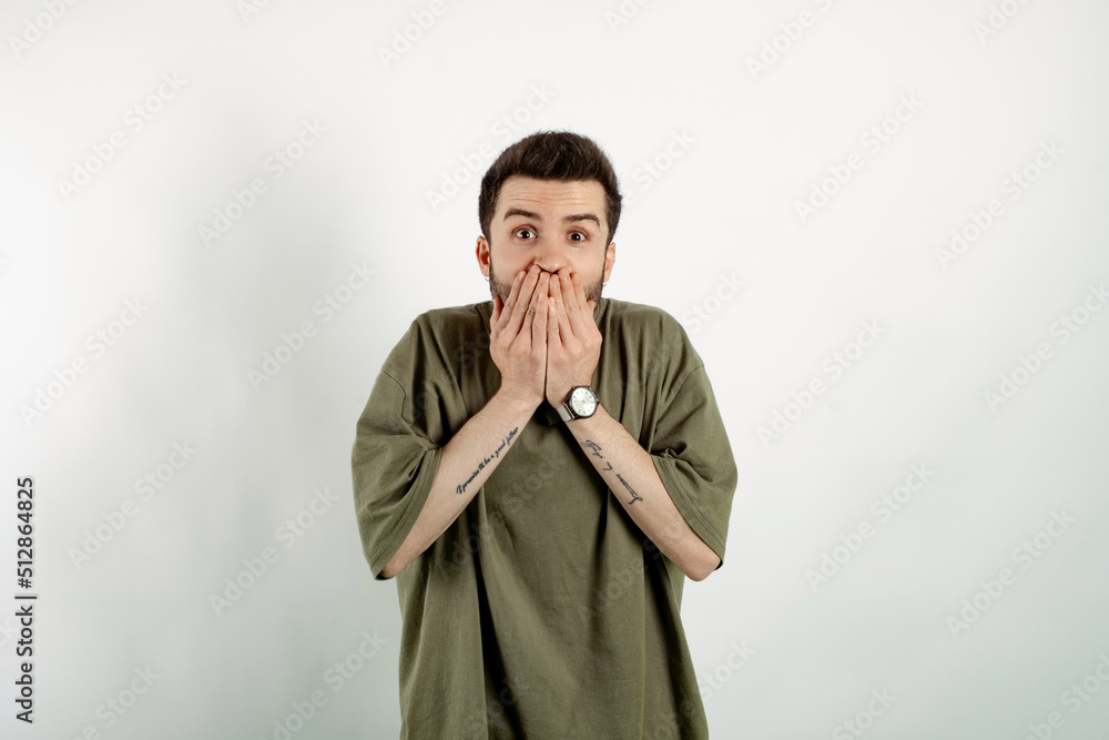 Portrait of casual young man wearing casual clothes posing isolated over white background shocked covering mouth with hands for mistake while. Secret concept. Looking at the camera. Portrait of casual young man wearing casual clothes posing isolated over white background shocked covering mouth with hands for mistake while. Secret concept. Looking at the camera.