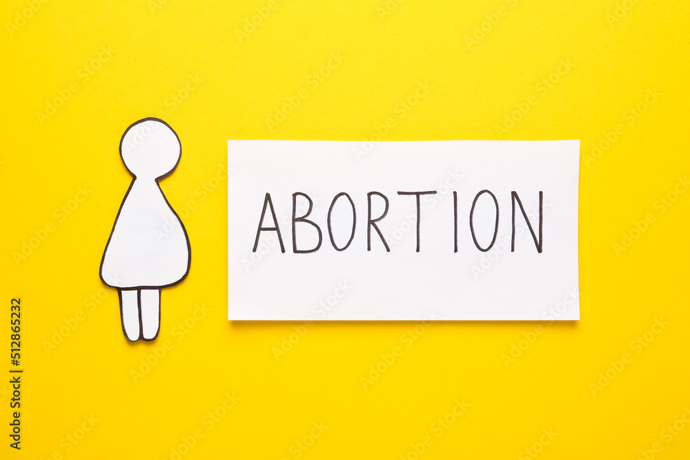 Note with word Abortion and pregnant woman paper cutout on yellow background, flat lay Note with word Abortion and pregnant woman paper cutout on yellow background, flat lay