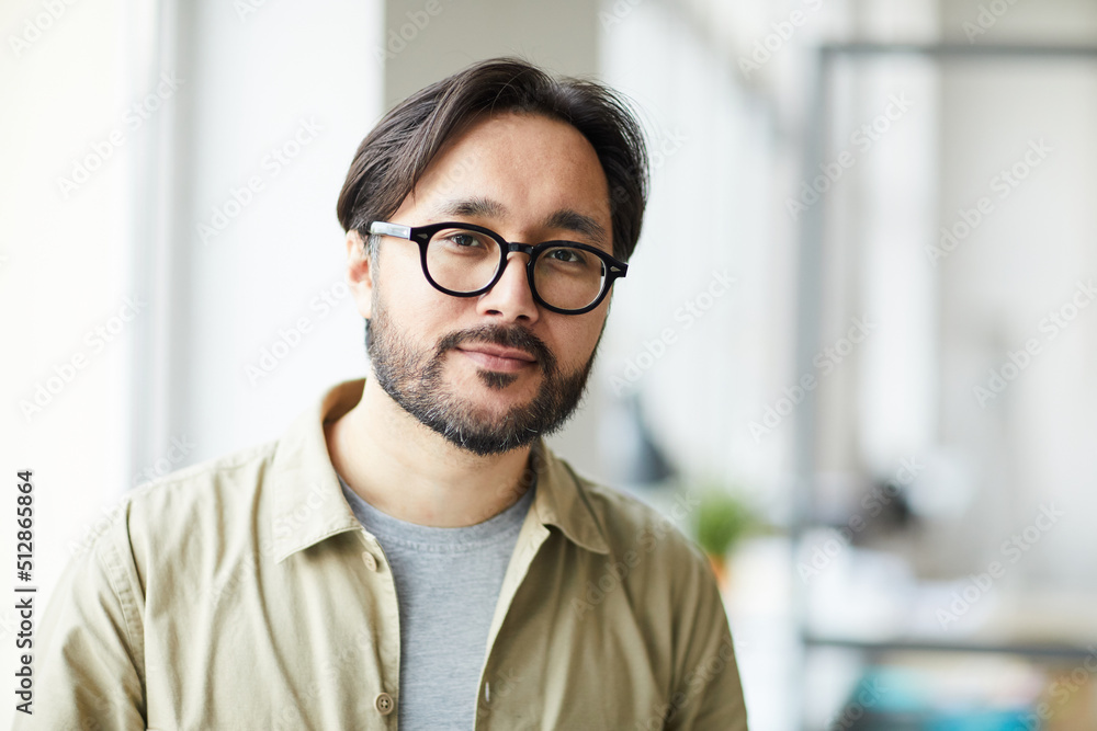 Portrait of content handsome young Asian employee with stylish beard working in modern office without corporate style Portrait of content handsome young Asian employee with stylish beard working in modern office without corporate style