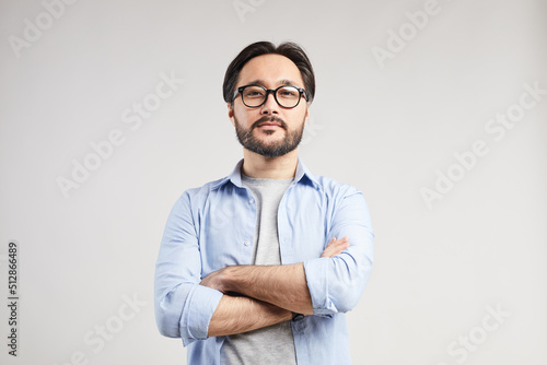 Serious confident young Asian web designer with black beard standing against isolated background and looking at camera © Mediaphotos