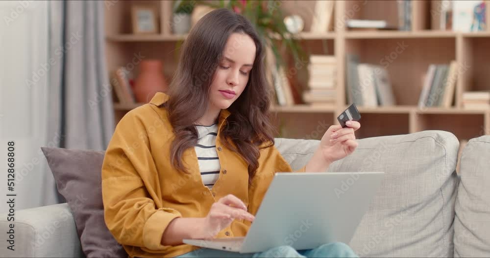 Happy caucasian woman using laptop and credit card in hands sitting on sofa at home. Lady celebrating victory. Female using instant mobile payments making purchase in online store. E-banking service. Happy caucasian woman using laptop and credit card in hands sitting on sofa at home. Lady celebrating victory. Female using instant mobile payments making purchase in online store. E-banking service.