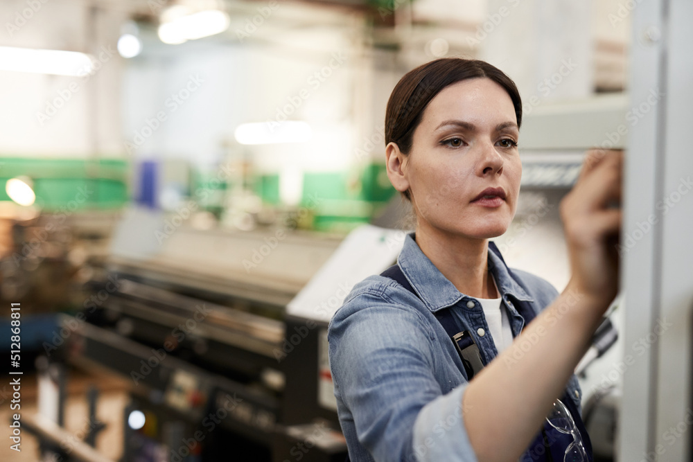 Busy focused brunette female factory engineer standing in modern industrial shop and choosing program on cnc lathe Busy focused brunette female factory engineer standing in modern industrial shop and choosing program on cnc lathe