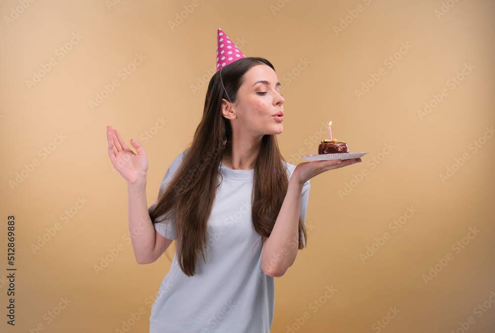Happy young cheerful birthday girl with a present wearing party head on a beige background. Happy young cheerful birthday girl with a present wearing party head on a beige background.