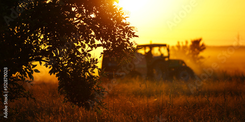 Making hay - tractor on a pasture against the setting sun 