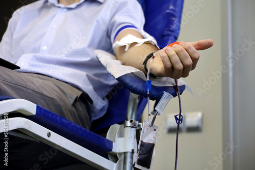 Man blood donor in chair during donation with a blood bag and red bouncy ball in hand, selective focus. Concept of donorship, transfusion, health care