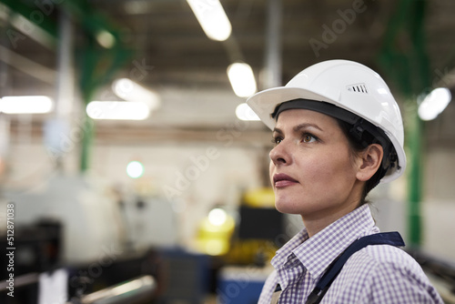Obraz na plátně Serious purposeful young female engineer in white hardhat standing in workshop o