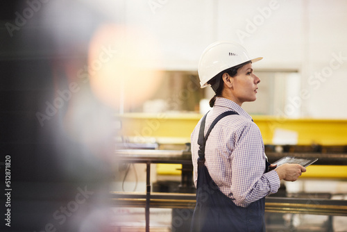 Rear view of serious female assembly line worker in hardhat standing at conveyor and controlling movement of produced details