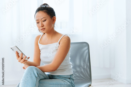 Wary irritated angry tanned lovely young Asian woman read bad news at call using phone at home interior living room. Distance communication Social media concept. Cool offer Banner Wide angle