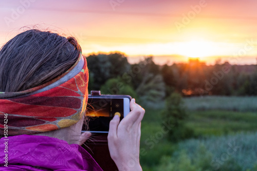 The photo of a girl from behind taking photo of a sunset