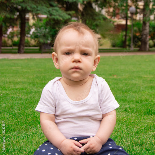 The child sits on the grass alone. Baby is sad and wants to cry