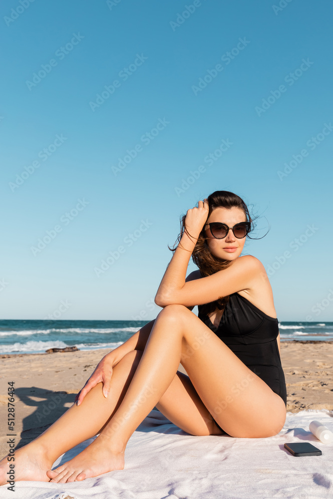 young woman in swimwear and sunglasses sitting blanket near sea. young woman in swimwear and sunglasses sitting blanket near sea.