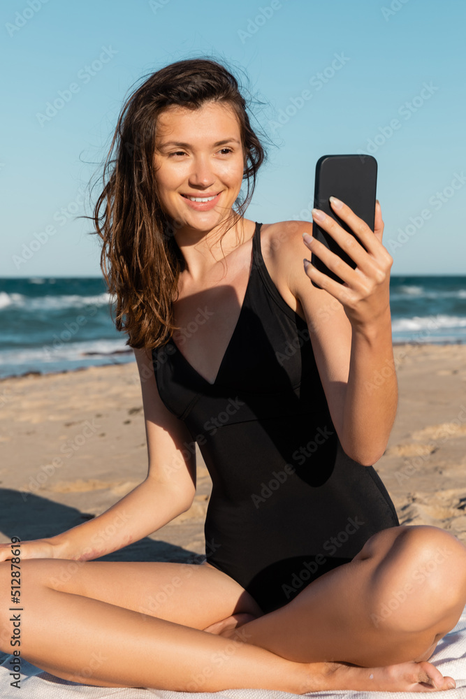 happy young woman in swimsuit taking selfie on smartphone near sea.