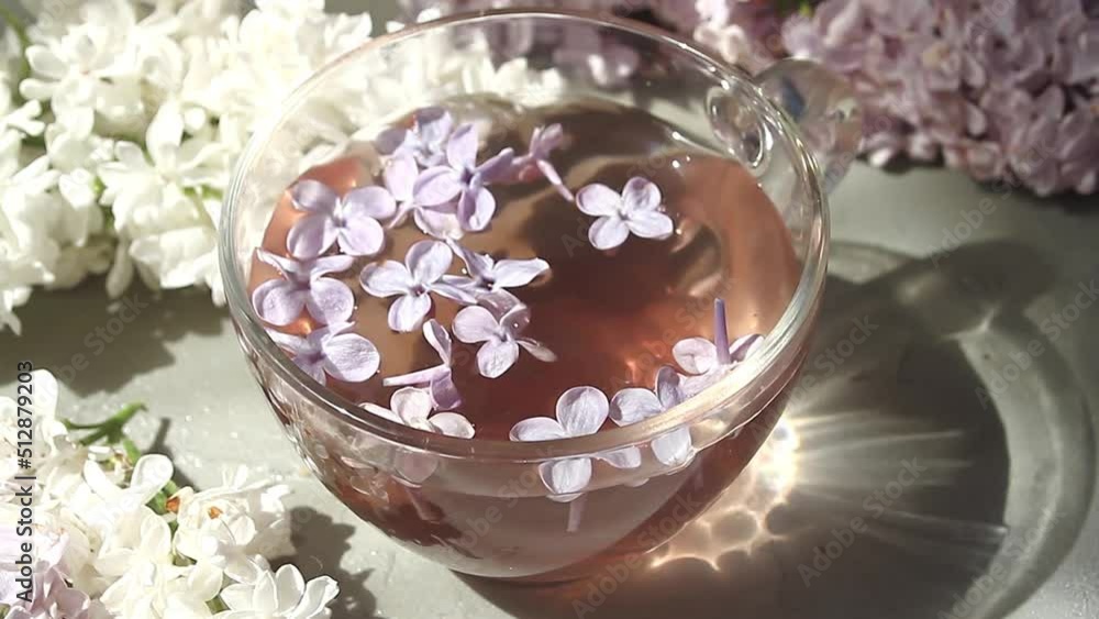 Lilac flowers fall into a glass cup with tea, an infusion of lilac. The sunbeam shines on the cup. Light and shadows. High quality FullHD footage Lilac flowers fall into a glass cup with tea, an infusion of lilac. The sunbeam shines on the cup. Light and shadows. High quality FullHD footage