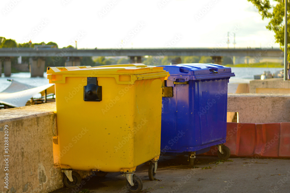 Yellow and blue garbage bin stand on the embankment in the city. Yellow and blue garbage bin stand on the embankment in the city.