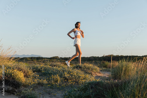 brunette and fit woman in shorts and sports bra listening music and running outside.