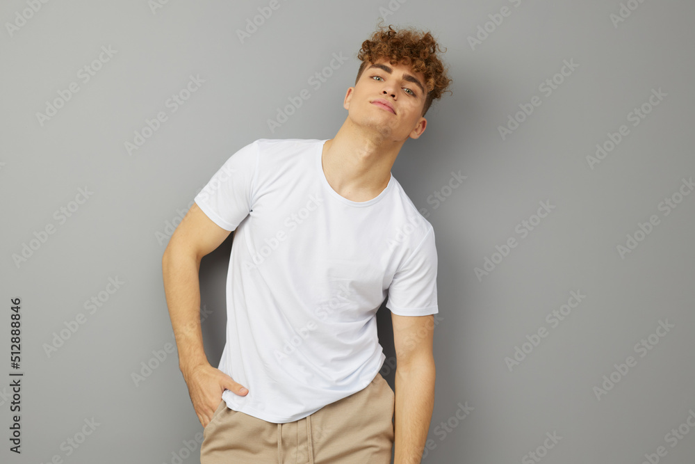 a relaxed, handsome man with curly hair stands on a gray background in a casual white T-shirt, looking pleasantly at the camera. Studio photography a relaxed, handsome man with curly hair stands on a gray background in a casual white T-shirt, looking pleasantly at the camera. Studio photography