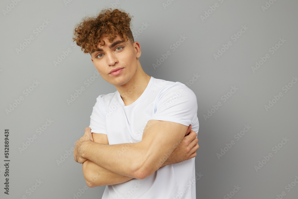 a relaxed, handsome man stands on a gray background in a casual white T-shirt with his arms folded on his chest. Horizontal Studio Photography a relaxed, handsome man stands on a gray background in a casual white T-shirt with his arms folded on his chest. Horizontal Studio Photography