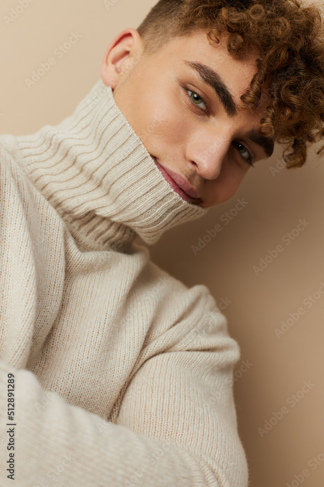 a handsome, attractive man with curly hair stands on a beige background in a light turtleneck pulled over his face, looking pleasantly into the camera a handsome, attractive man with curly hair stands on a beige background in a light turtleneck pulled over his face, looking pleasantly into the camera