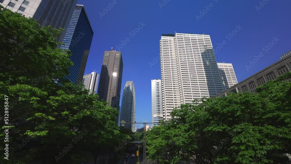 Nishi-Shinjuku skyscraper stands beyond fresh green trees growing on the Chuo-Dori Avenue beneath elevated walkway in Shinjuku subcenter district at Shinjuku, Tokyo, Japan on May 04, 2022. Nishi-Shinjuku skyscraper stands beyond fresh green trees growing on the Chuo-Dori Avenue beneath elevated walkway in Shinjuku subcenter district at Shinjuku, Tokyo, Japan on May 04, 2022.