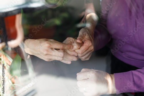 Mid Adult Woman Care Giver Helps Senior Woman to Remove some Thorns from Her Hands at Window better Light in Domestic Environment