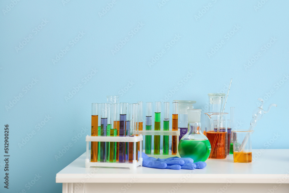 Different laboratory glassware with samples on table near blue wall Different laboratory glassware with samples on table near blue wall
