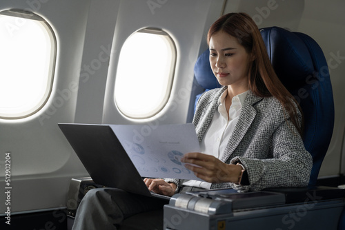 Asian young woman using laptop with financial report sitting near windows at first class on airplane during flight  Traveling and Business concept