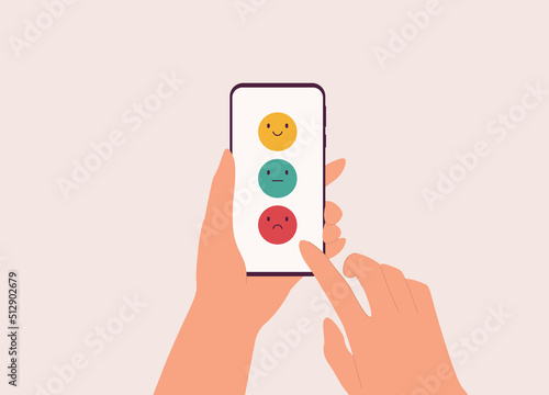 One Person’s Hand Holding Mobile Phone With Happy, Neutral and, Angry Face Emoji On Screen Submitting Review Or Feedback. Close-Up. Character, Cartoon. photo