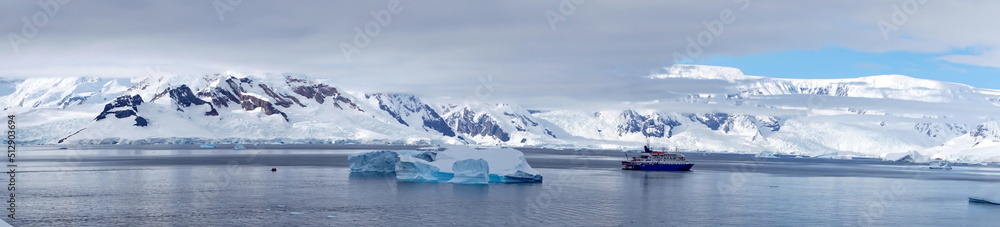 Panorama of an expedition cruise ship in a bay, surrounded by icebergs, at Portal Point, Antarctica