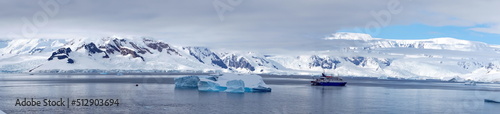Panorama of an expedition cruise ship in a bay, surrounded by icebergs, at Portal Point, Antarctica © Angela