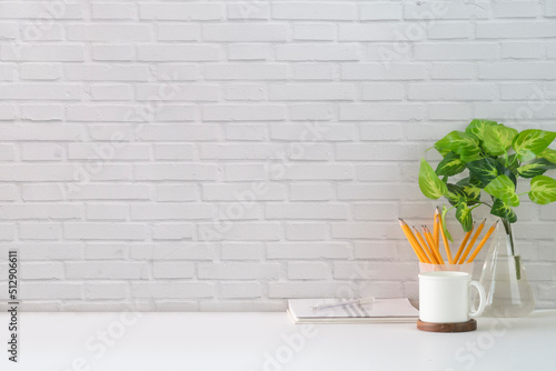 Comfortable workplace with blank picture frame, coffee cup, book and stationery on white table against brick wall. Copy space for your text. © wattana