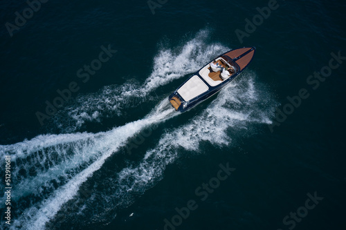 Luxurious wooden boat fast movement on dark water..Classic Italian wooden boat fast moving aerial view. Top view of a wooden powerful motor boat. © Berg