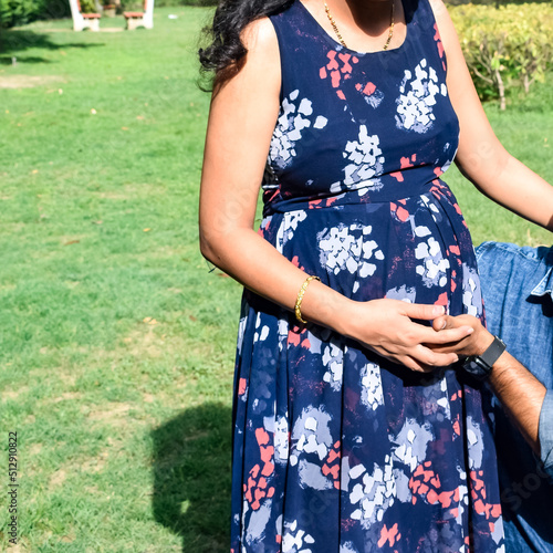 Indian couple posing for maternity baby shoot. The couple is posing in a lawn with green grass and the woman is falunting her baby bump in Lodhi Garden in New Delhi, India