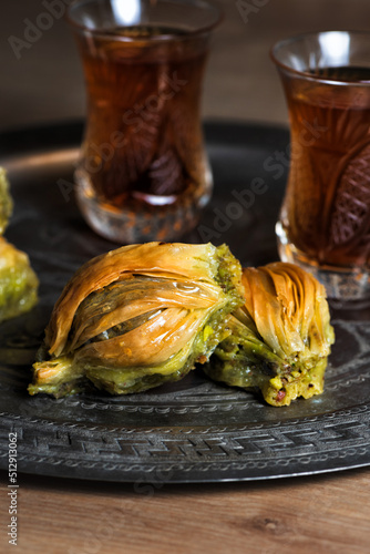 Turkish pistachio baklava on traditional metal tray. Pastry dessert with nuts and tea on wooden table