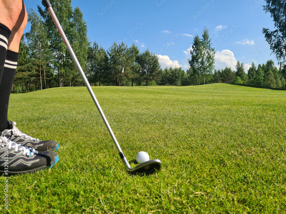Obraz premium Closeup of white golf ball and club. Human feet on green grass