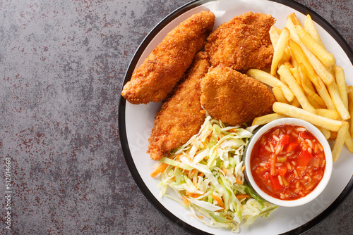 Photos Serbian fried chicken with French fries, cabbage salad and hot sauce close up in the plate on the table