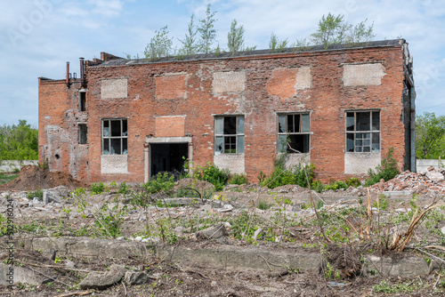 Old industrial workshop made of red brick, dilapidated, in disrepair with broken windows and doors against background of blue summer sky
