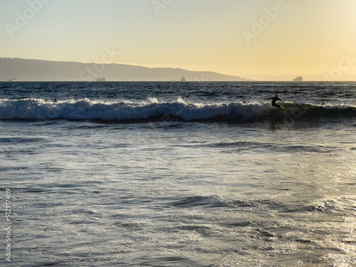 Man silhouette surfing waves at sunset on the beach with cargo ships by Valparaiso harbor on background in Chile. Summer water sport concept