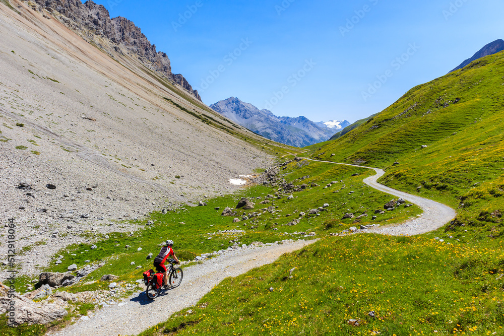 Man tourist cycling on mtb bike with luggage in panniers in beautiful Alpisella valley on sunny summer day, Alps Mountains, Italy