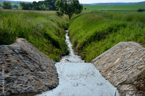 stone lining of bank at the mouth of the sewer pipe with a grate against the entry of persons into the treatment plant or industrial building. leftover toilet paper was trapped on the grille photo