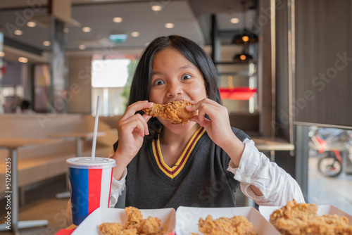 Close up portrait of a satisfied pretty  little asian girl eating fried chicken and french fries In the restaurant. Unhealthy food concept  close up