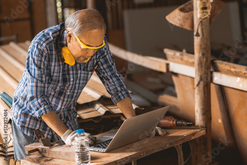 Senior builder wood worker using laptop computer at aiding design at construction work.
