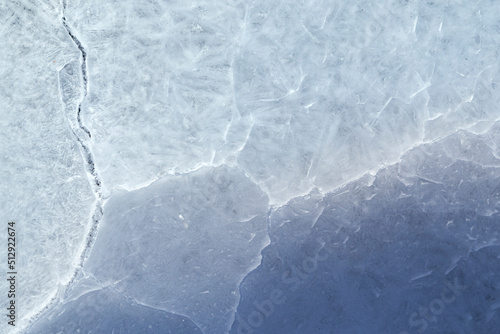 Close-up of cracked ice on a frozen lake in the winter, viewed from above. Abstract textured full frame background. Copy space, top view.