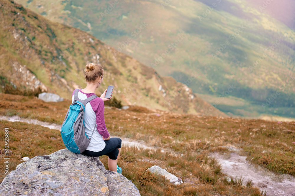 Naklejka premium Modern technology and communication. Be online in travel. hiking and trekking concept. Young woman with backpack using smartphone in the Carpathian mountains.