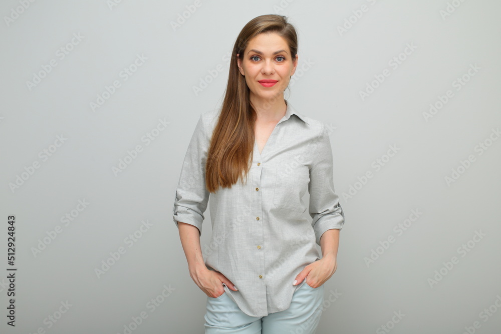 Smiling woman standing with hands in pockets, isolated female portrait, young lady dressed pants and gray shirt.